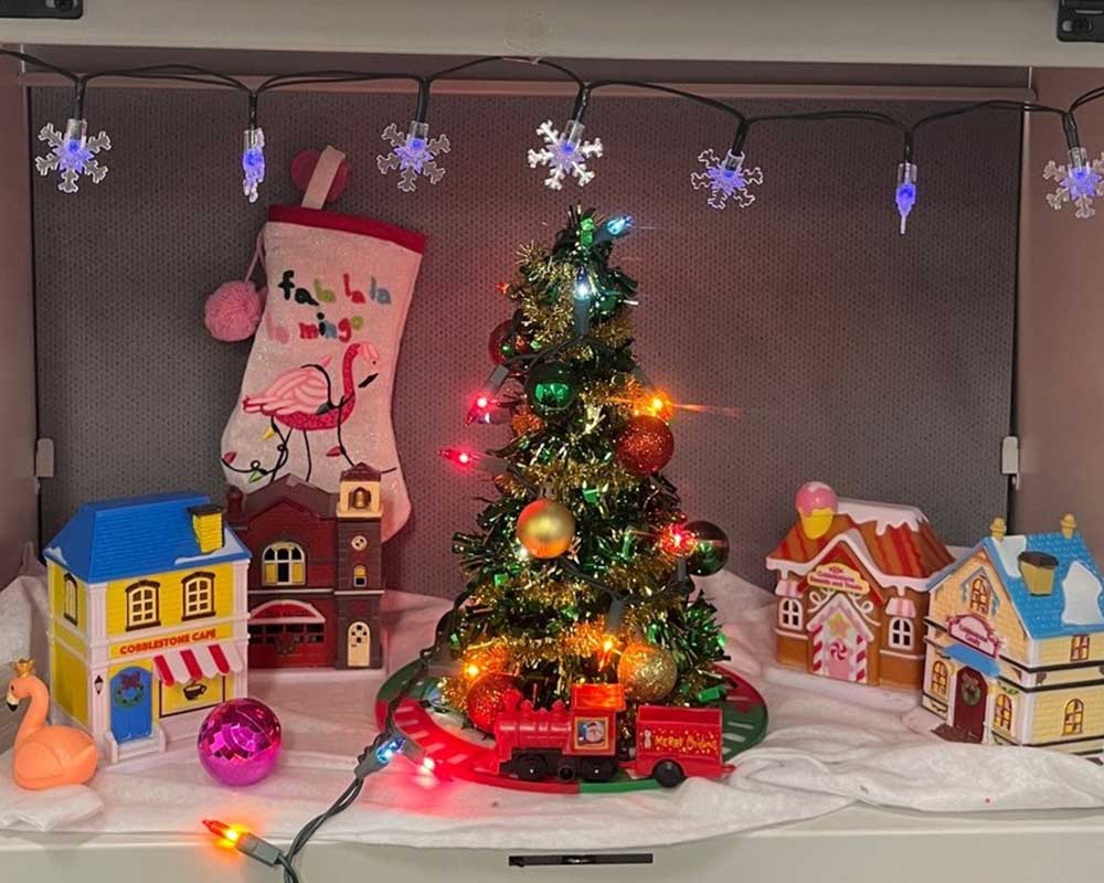 An office cubicle decorated with lights, a tree, and gingerbread houses for Christmas.