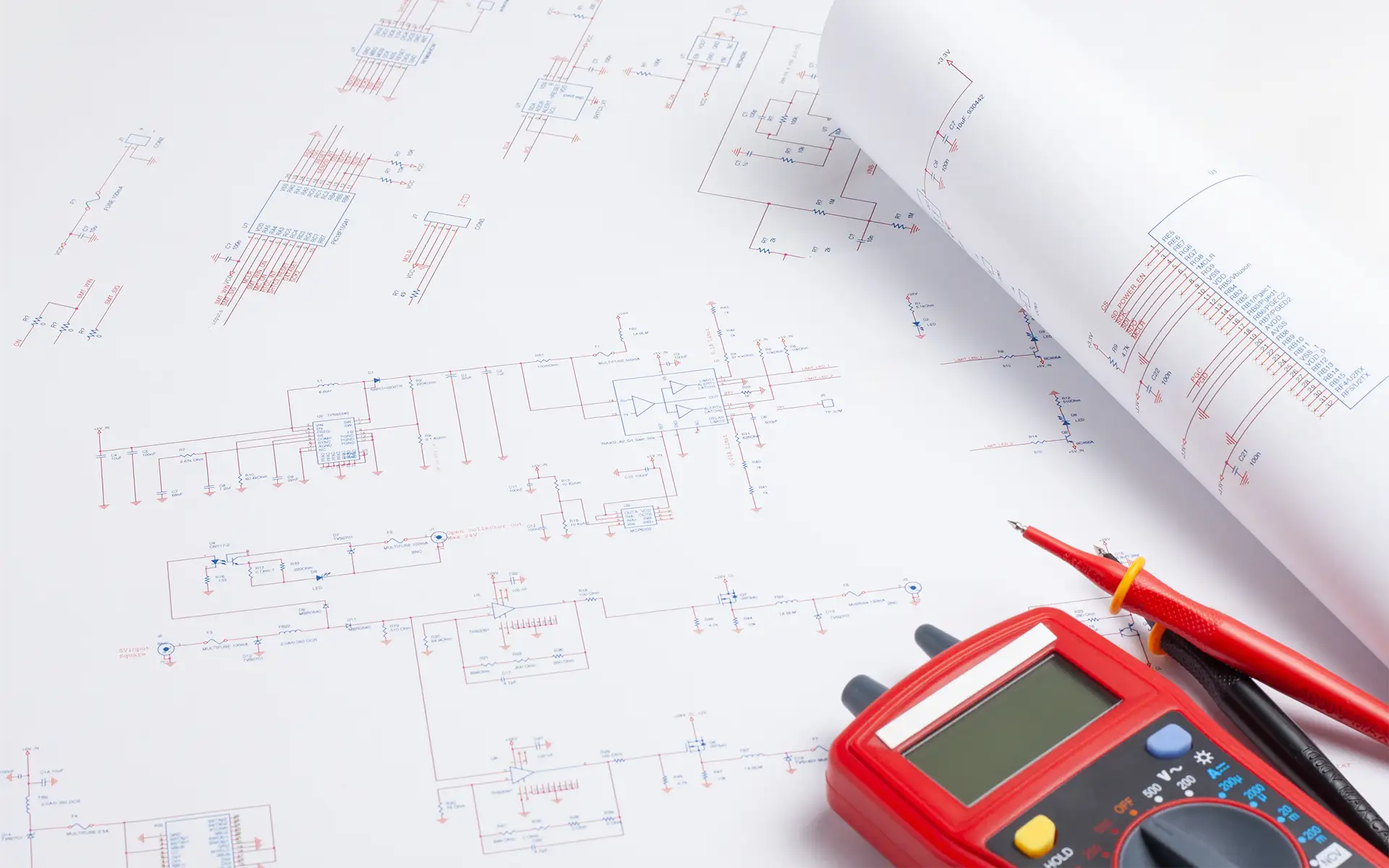 A red multimeter rests atop an unrolled white electrical circuit schematic as a relay selection is considered for the application