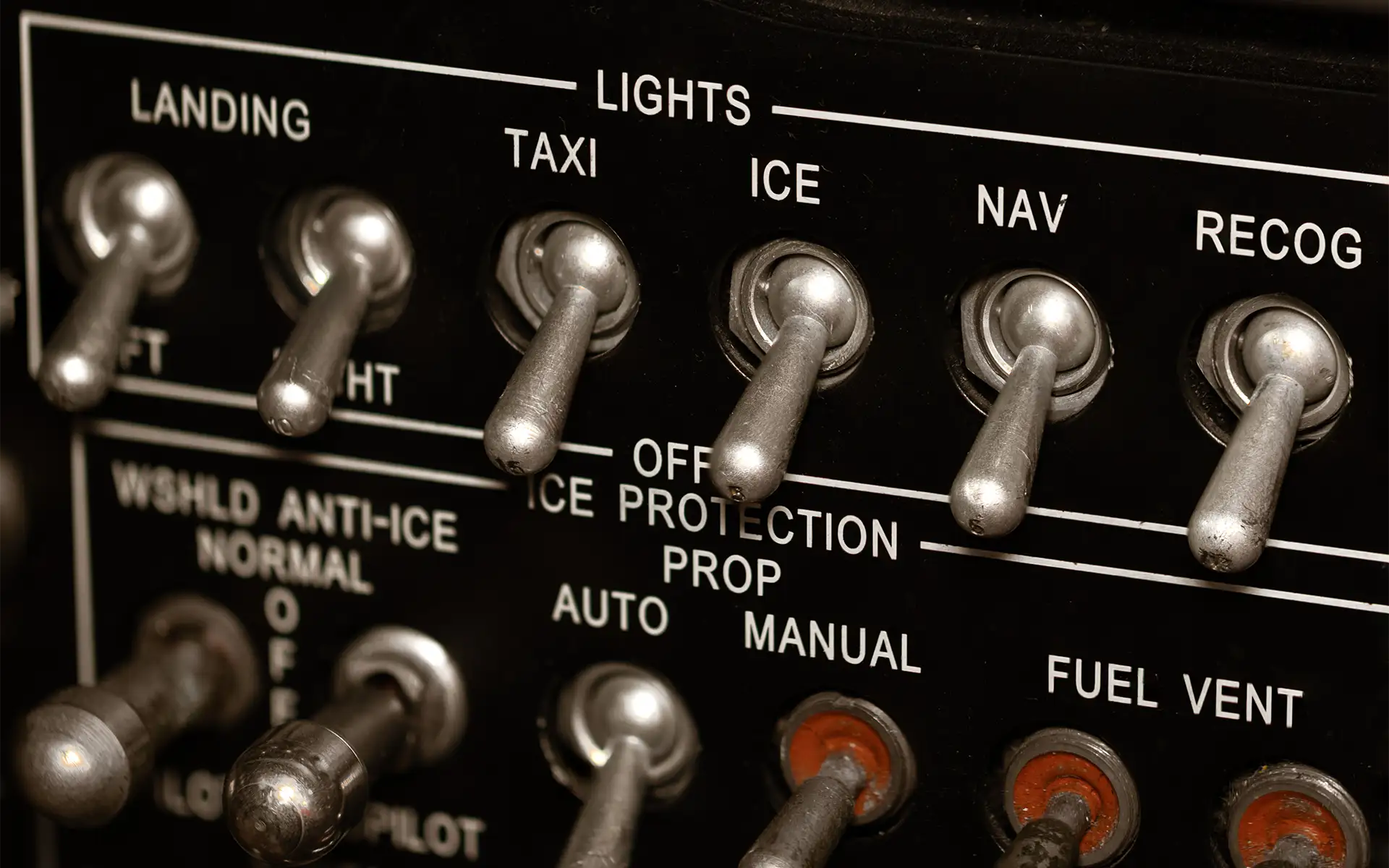 Close-up of a row of silver toggle switches on the lights panel in an airplane cockpit