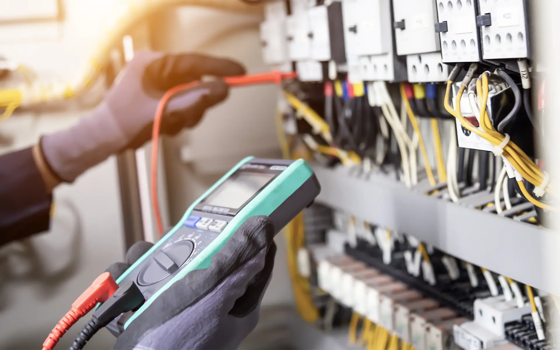An electrical inspector tests voltage in an industrial control panel using a voltage meter